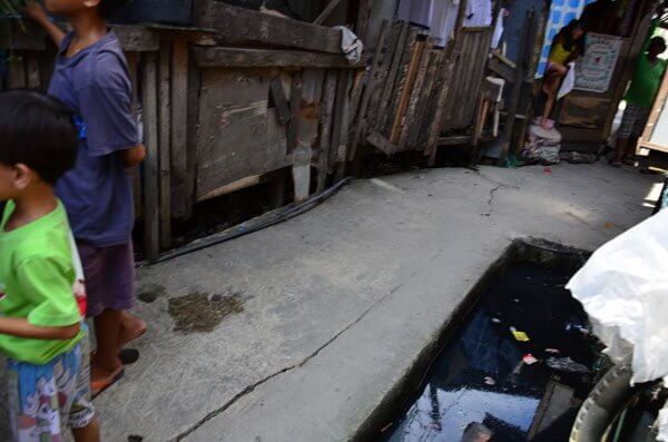 Canal of water to the right of the narrow alleyway in the slum.