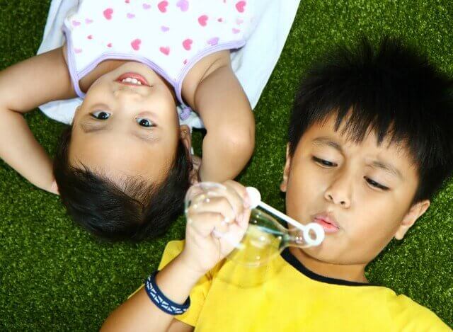 Two Kids Outside Lying And Playing On The Grass
