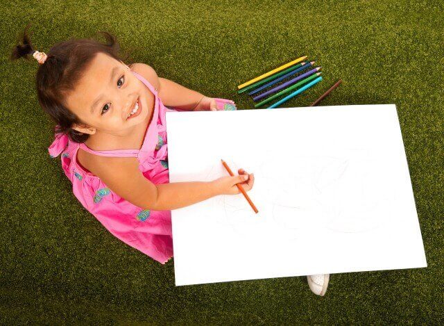 Child Sitting On The Grass Drawing A Picture With Multi Colorored Pencils